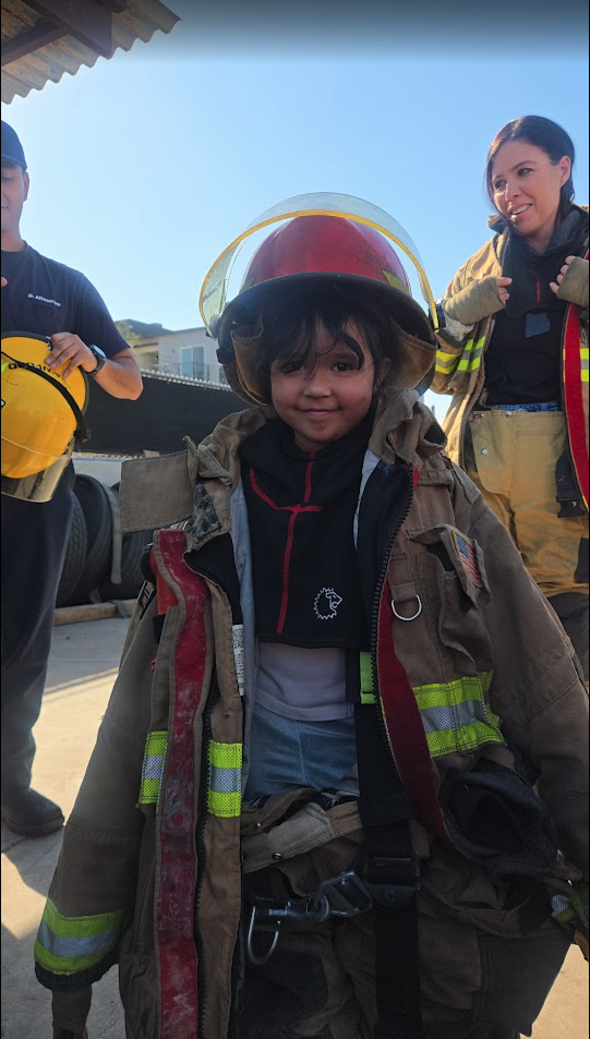 A child wearing firefighter gear during a community helpers visit