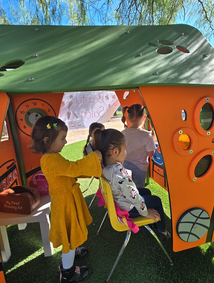 Two girls playing beauty salon in an outdoor dramatic play house
