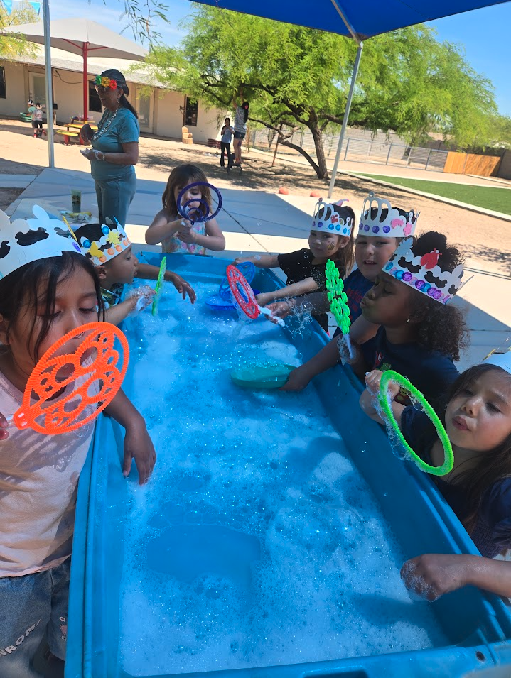 Children wearing crowns blowing bubbles at a foamy water table