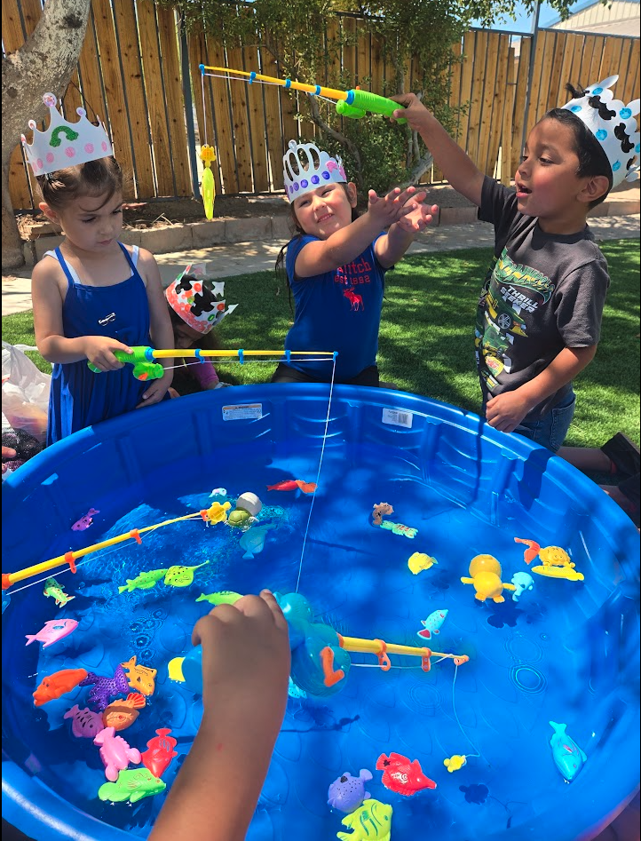 Children wearing crowns playing a magnetic fishing game at a water pool