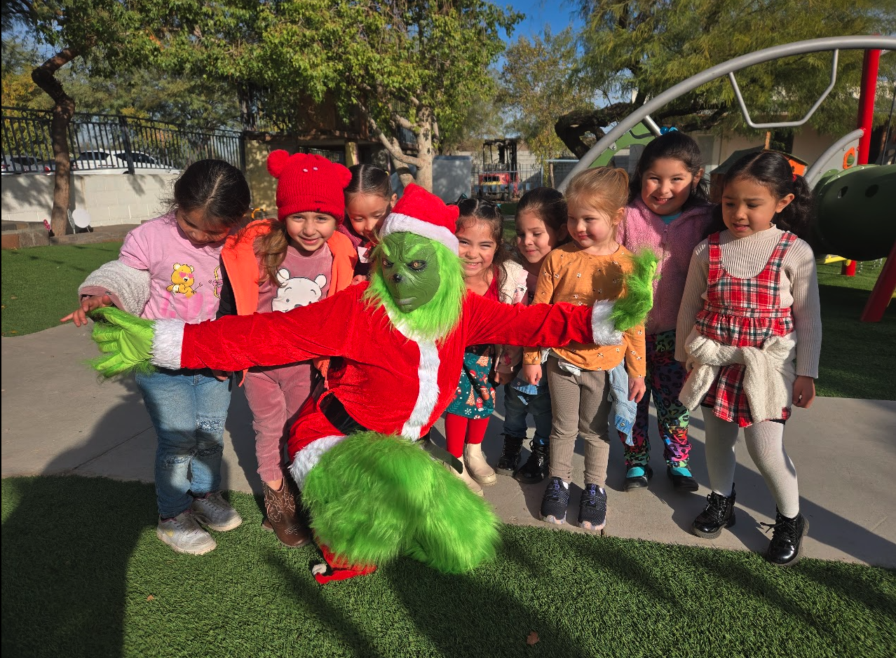 The Grinch in a Santa suit posing with a group of children on the playground