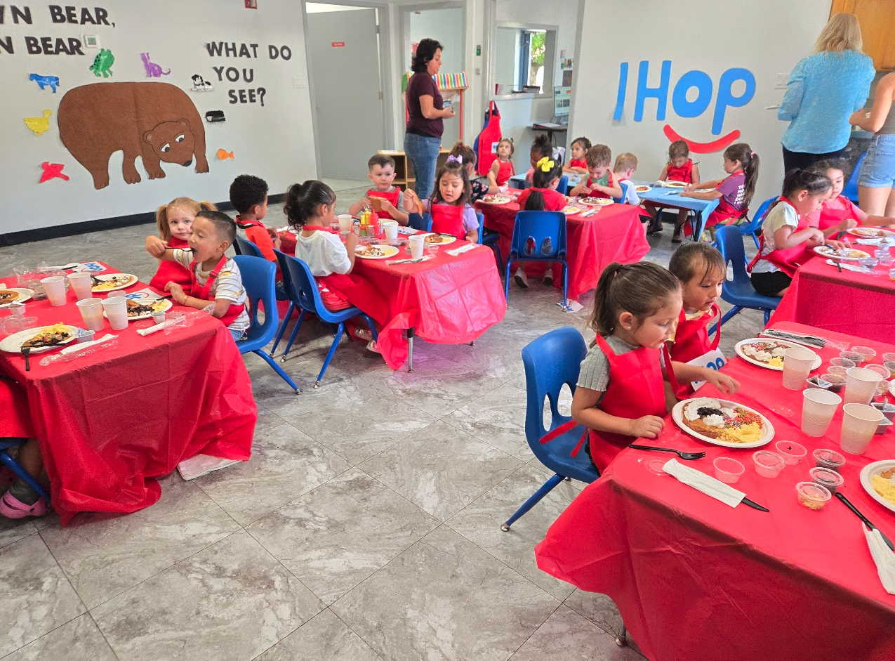 Children in red aprons eating pancakes at a breakfast event with a Brown Bear mural