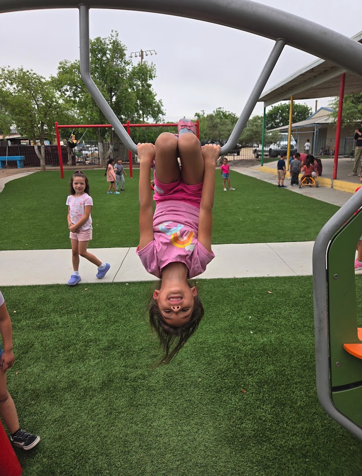 A child hanging upside down from the monkey bars while friends watch
