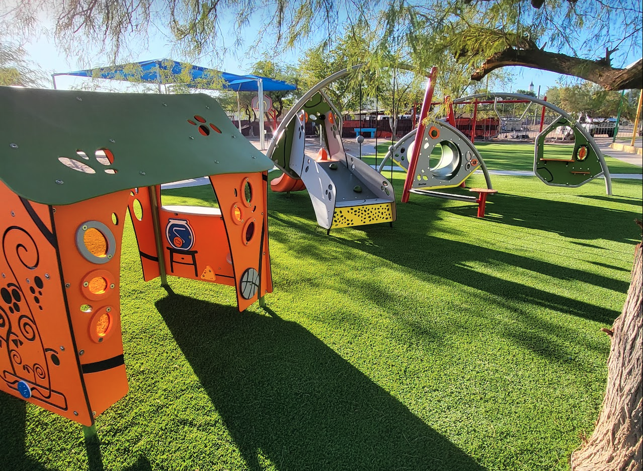 Colorful shaded playground with a playhouse, slide, and climbing structures on turf