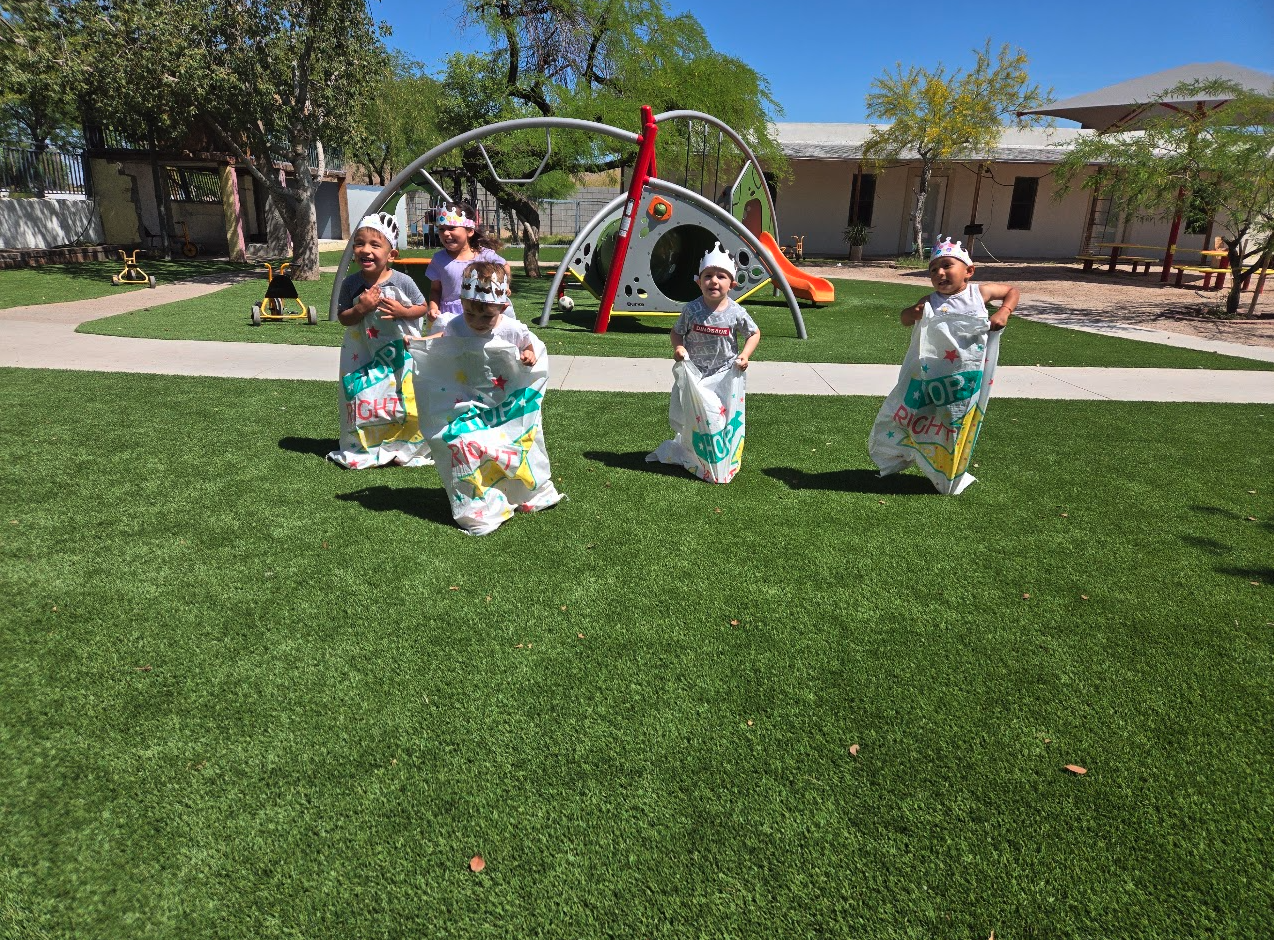 Children wearing paper crowns hopping in a potato sack race outside