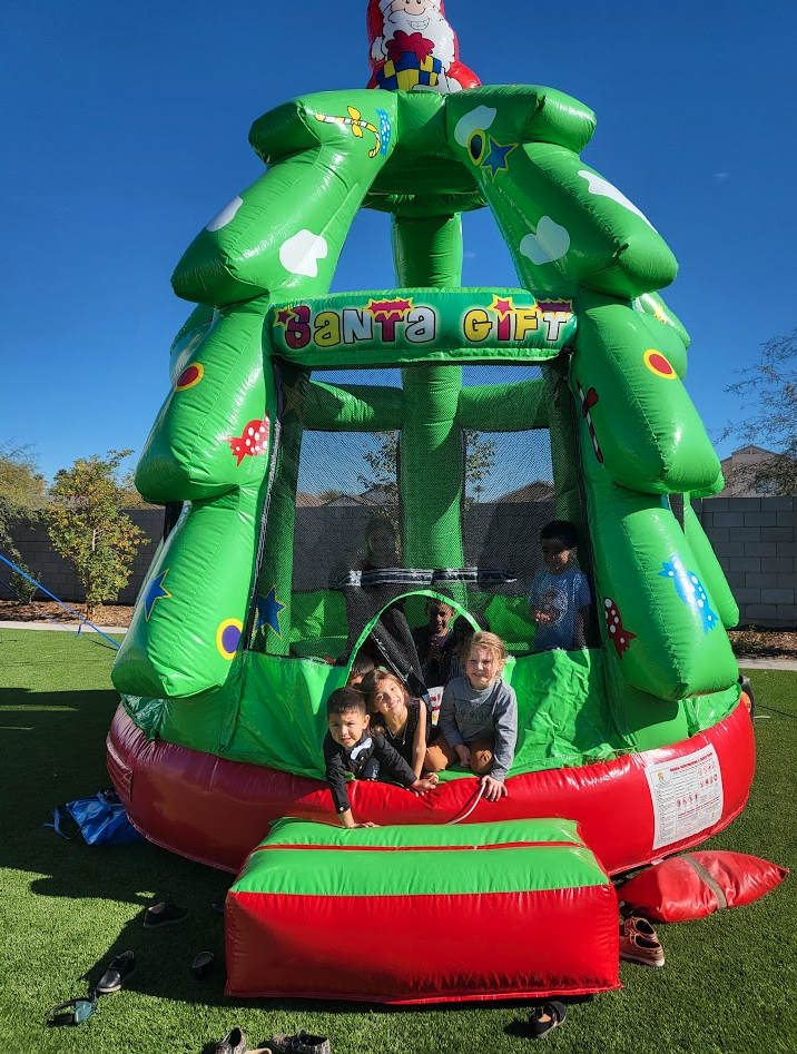 Children peeking out of a green Santa Gift Christmas tree bounce house