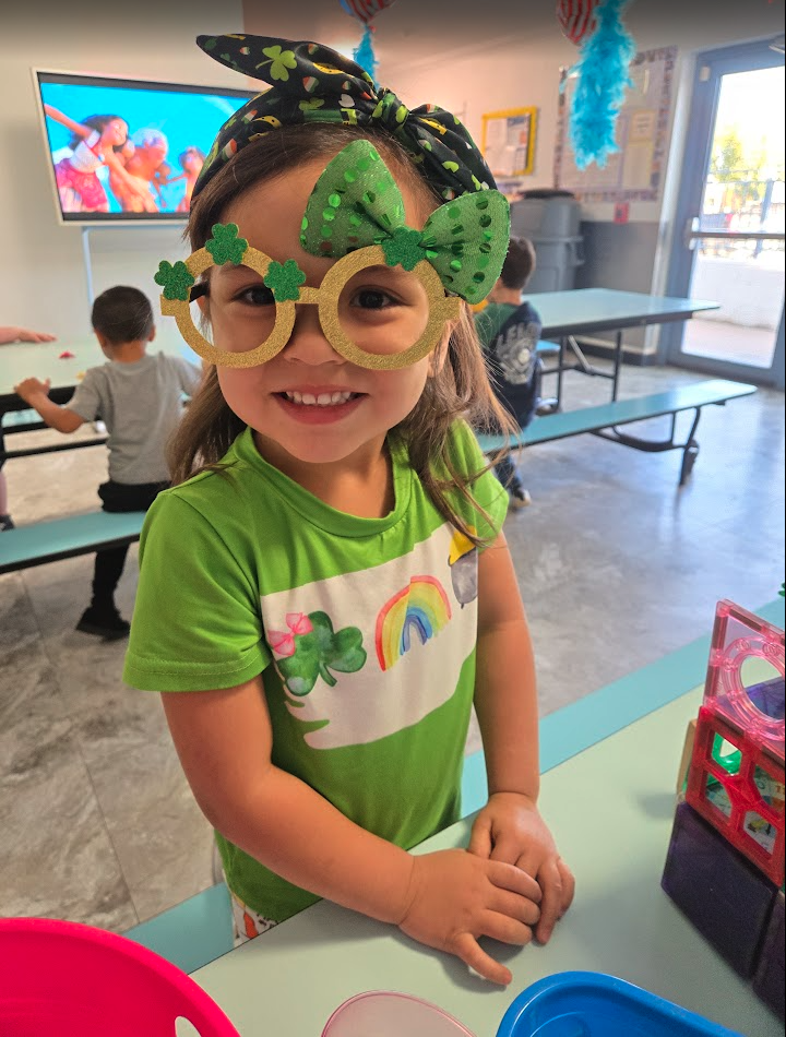 A smiling child wearing festive shamrock glasses in the classroom