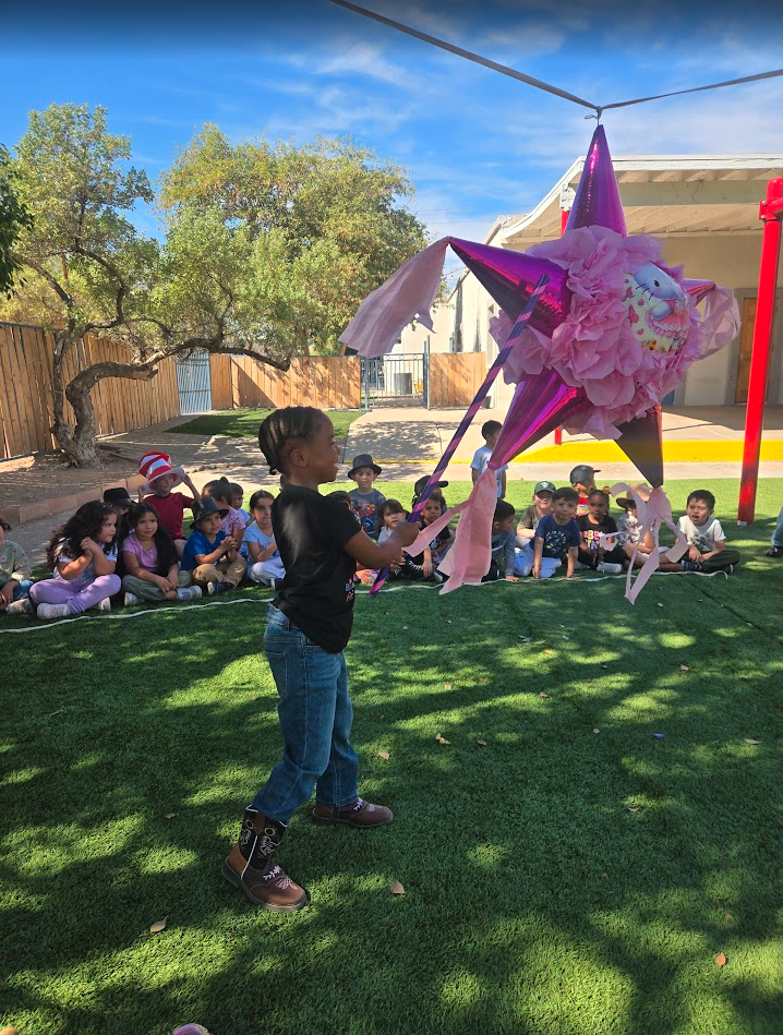 A child swinging at a star piñata while classmates watch outdoors